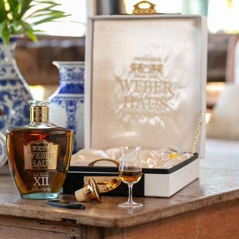 Cachaça Extra Premium Weber Haus XII Anos servida pura, ideal para harmonização com sobremesas sofisticadas. Ao fundo, embalagem da mesma.