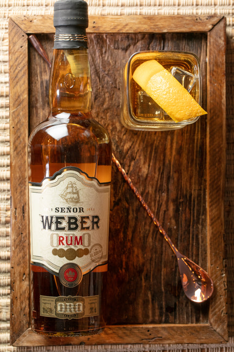 Garrafa de Rum Oro Señor Weber ambientada com um copo de drink.